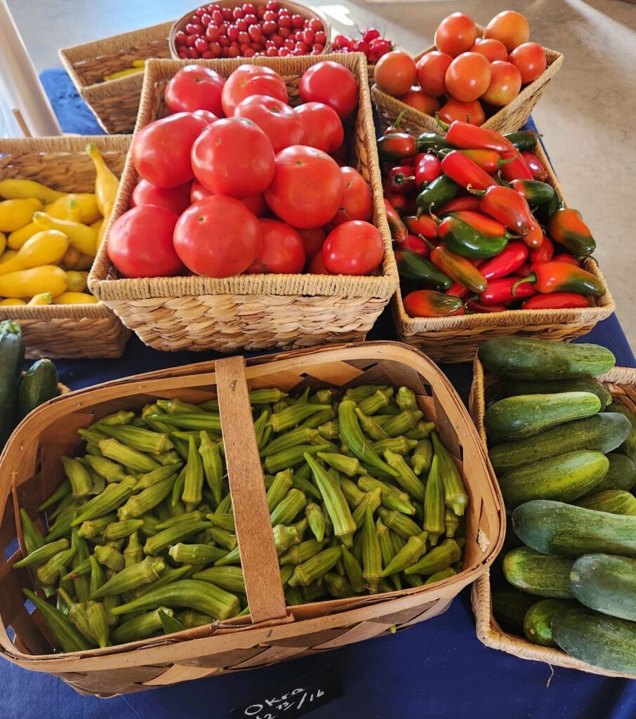 tower of baskets of fresh farm produce, like okra and tomatoes and peppers and cucumber and yellow squash