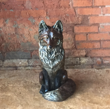 little bronze fox sculpture sitting on ground with brick background