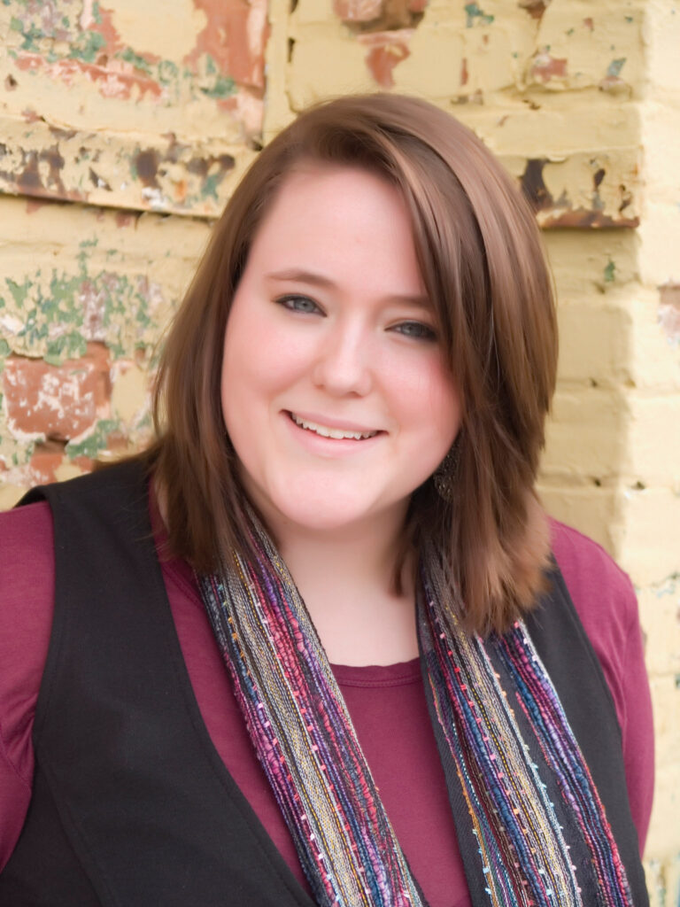Young woman smiling in front of brick building.