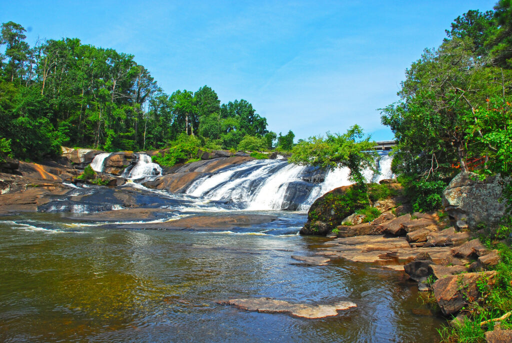 wide but short waterfall over rocks with green trees on either side