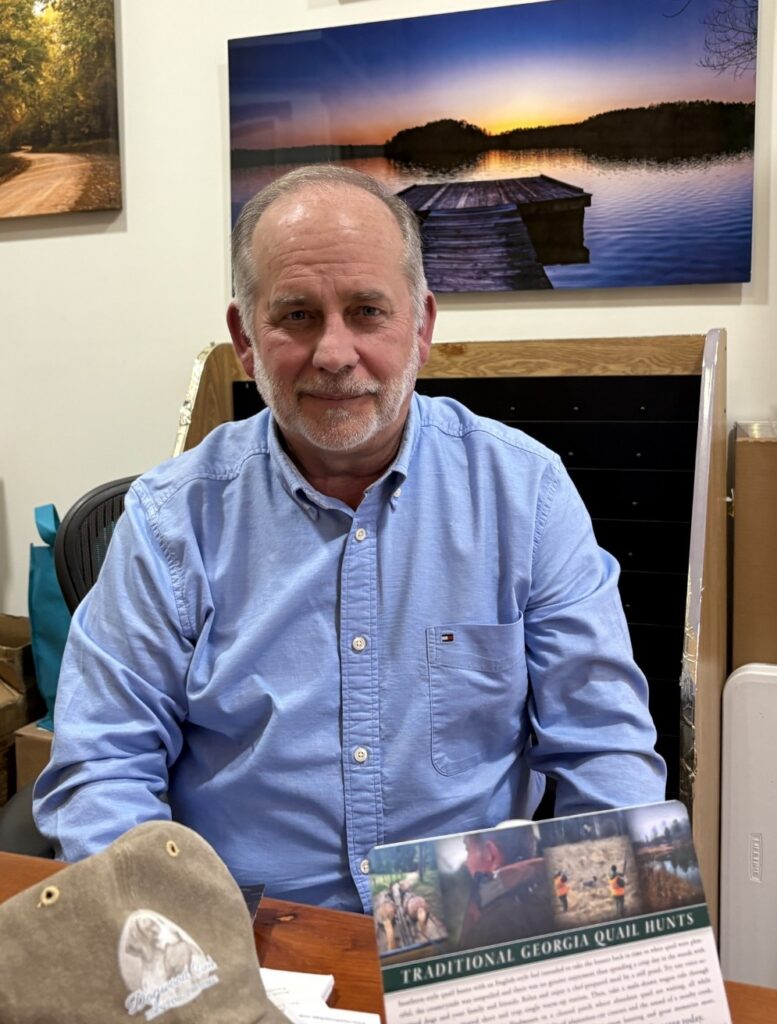 Older gentleman with gray hair and short-trimmed beard in blue shirt sits for portrait