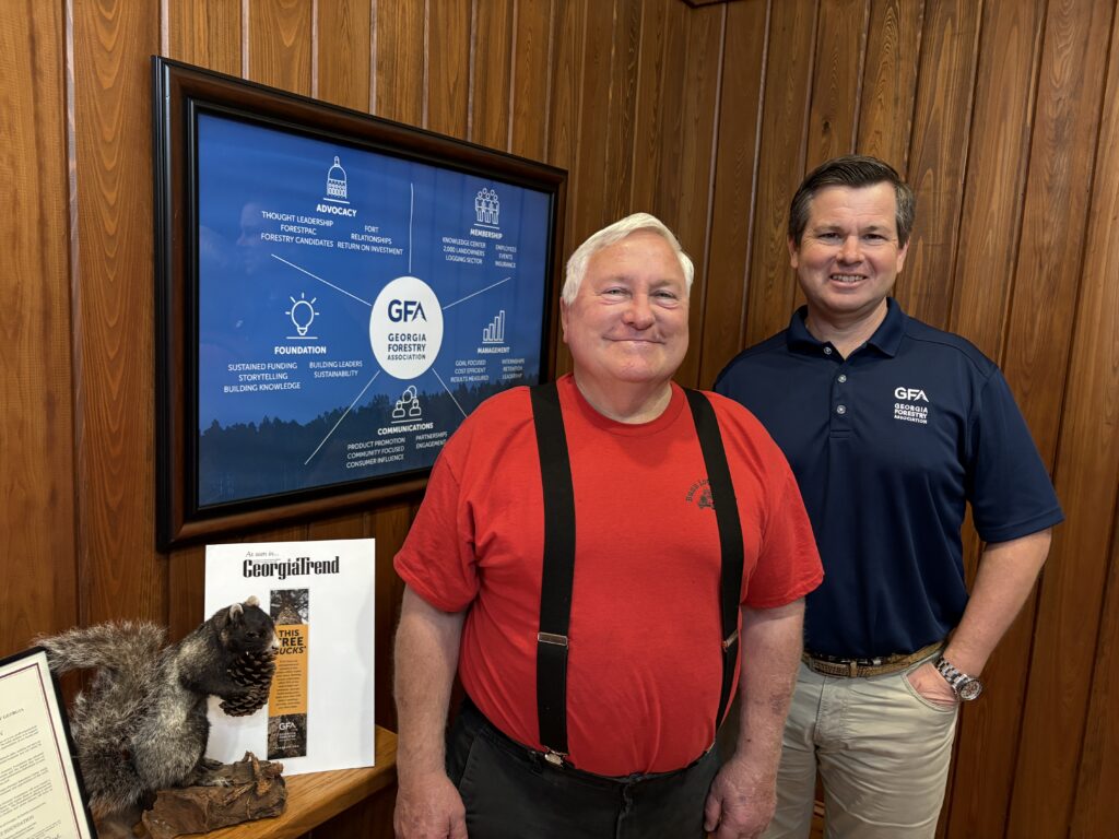 two men, one in red shirt and suspenders, other in navy polo, smile for the camera in a wood paneled room