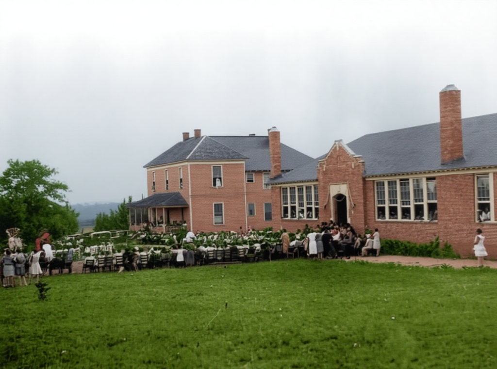 people gathered and seated on lawn in front of red brick buildings