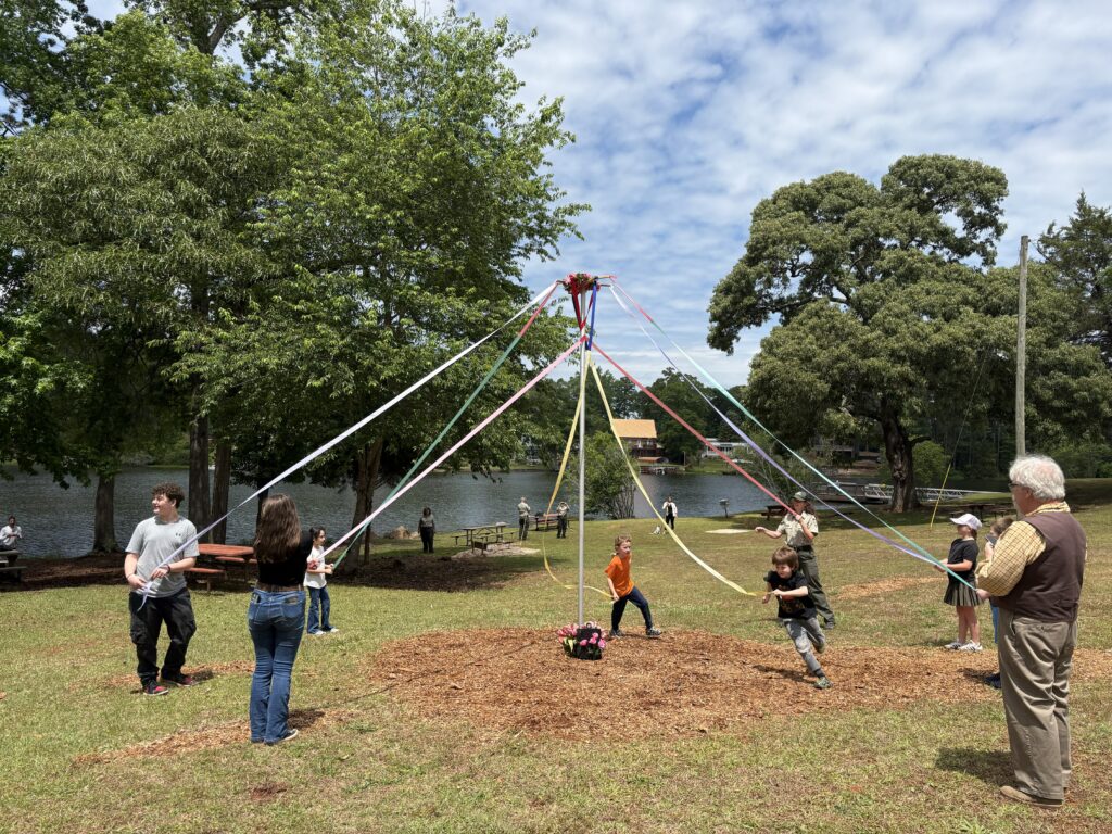 kids run around a may day pole with ribbons outside in park