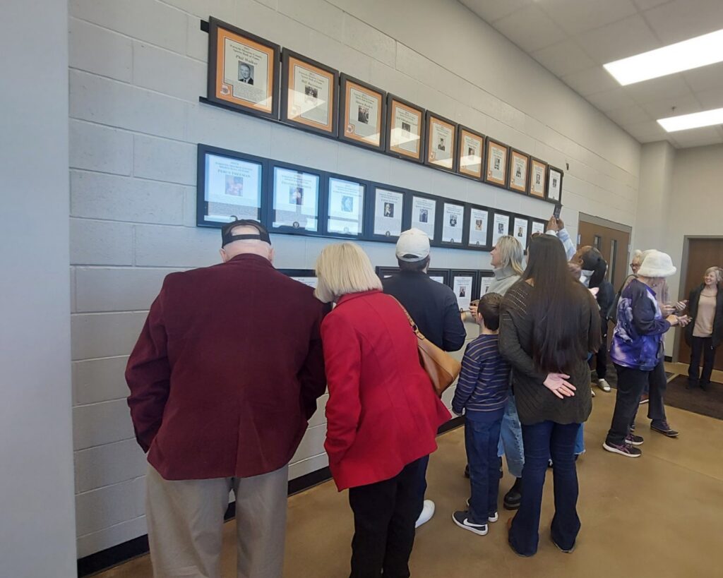 a crowd of people looking at plaques on a white wall