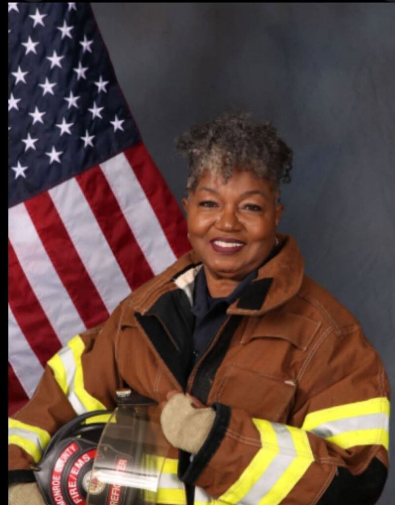 african american woman with short curly gray hair poses in firefighter uniform in front of american flag