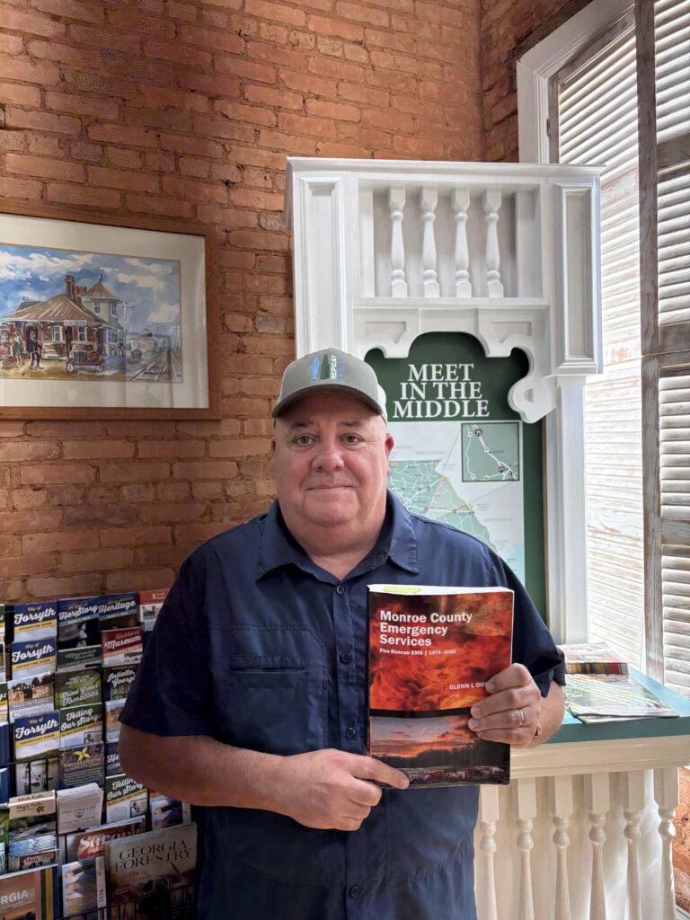 middle aged man in baseball cap holds book with picture of fire on cover