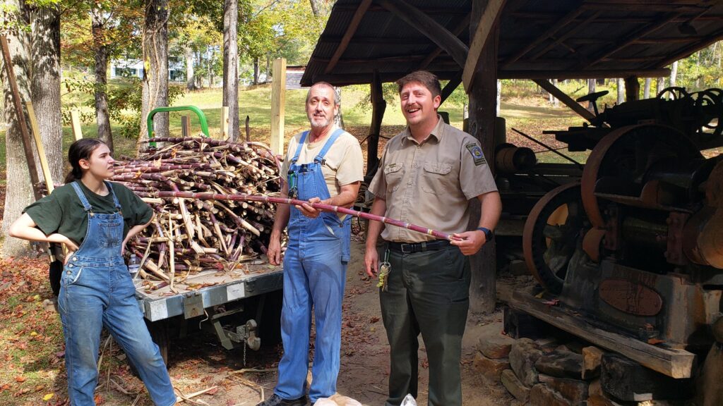 park ranger with a man and woman in overalls in front of an old pole barn with rusted equipment