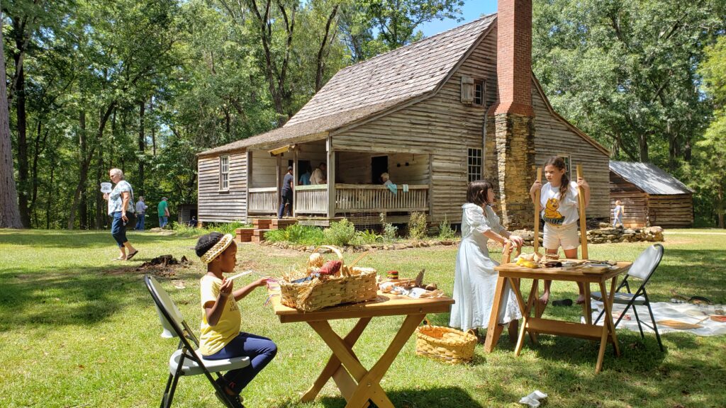 kids make crafts in yard in front of historic log house