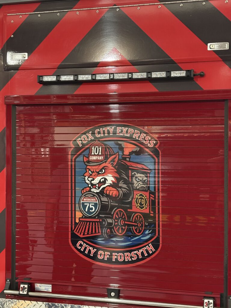 badge design with fox in firefighter uniform driving a train on back of truck