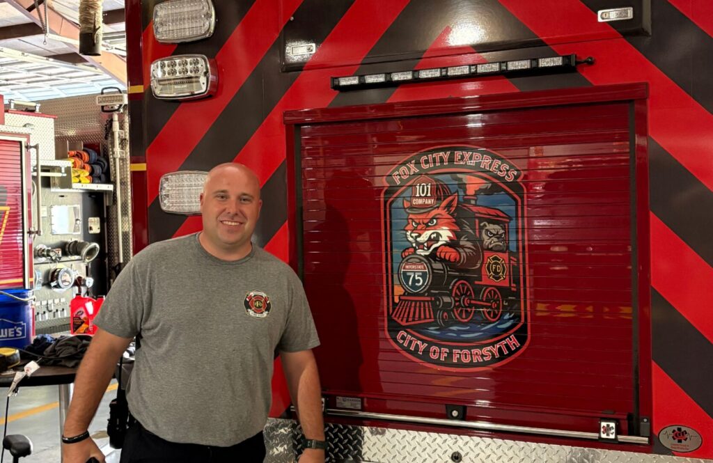 firefighter stands in front of back of ambulance with a large mural of a firefighting fox in a train on the back