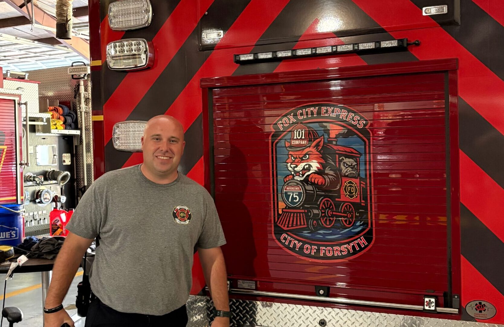 firefighter stands in front of back of ambulance with a large mural of a firefighting fox in a train on the back