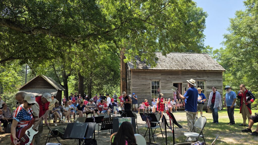 crowd gathers in front of old wooden cabin