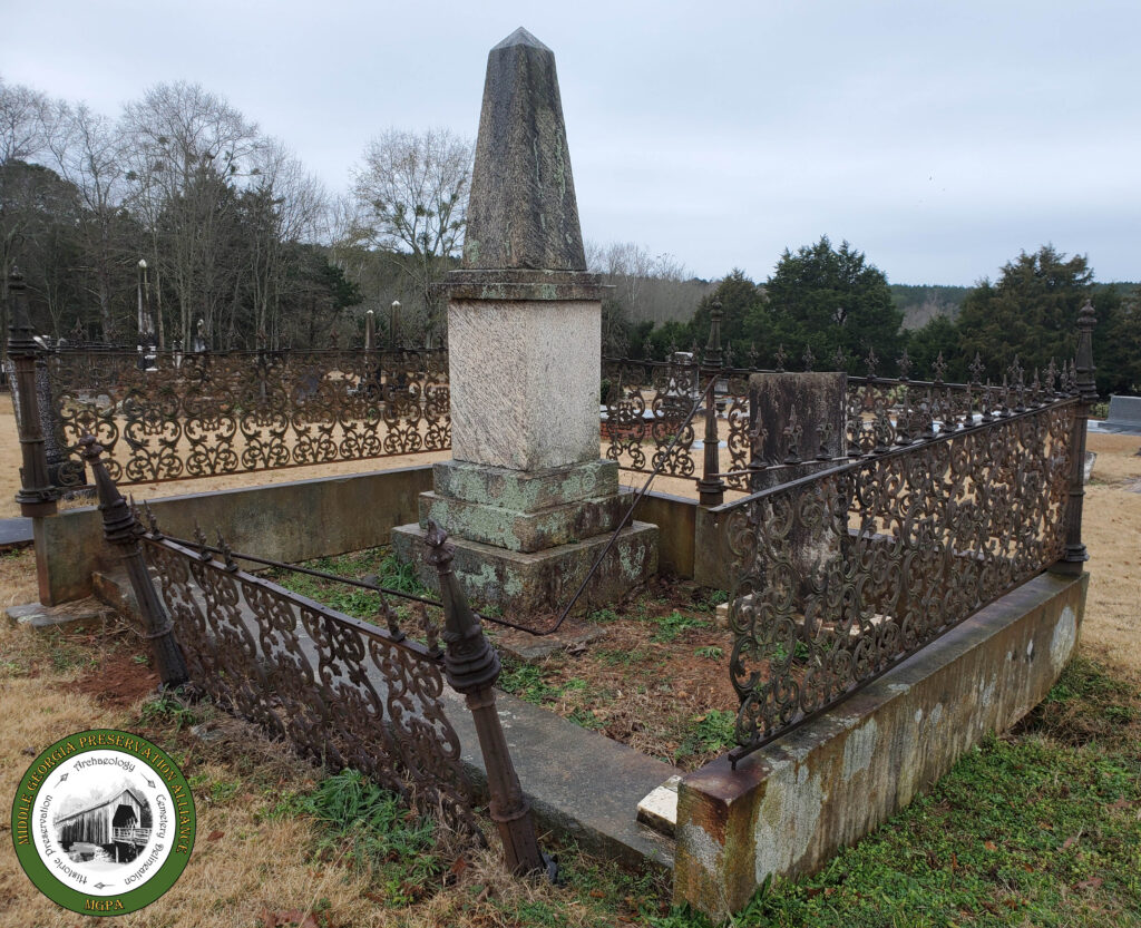 close up of a family burial plot fenced with an iron gate and large obelisk in the middle