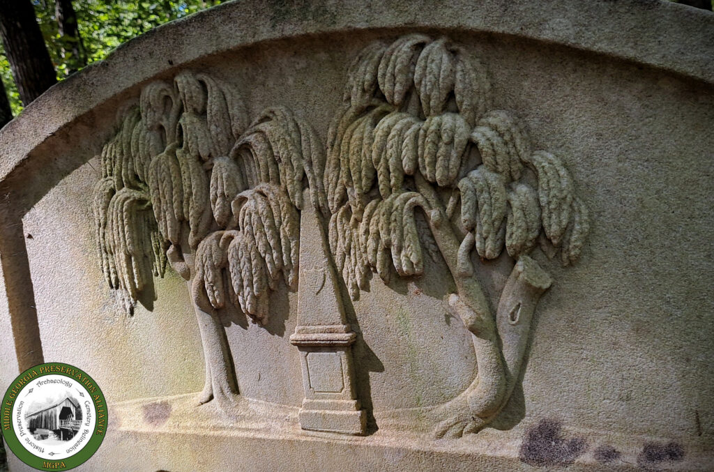 close up detail of headstone with carved willow trees overhanging a monument