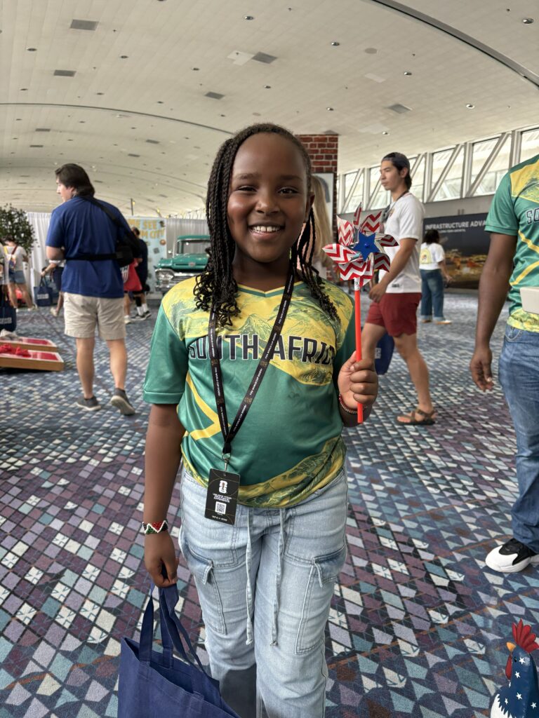 young girl from south africa poses in front of Visit Forsyth GA booth with pinwheel
