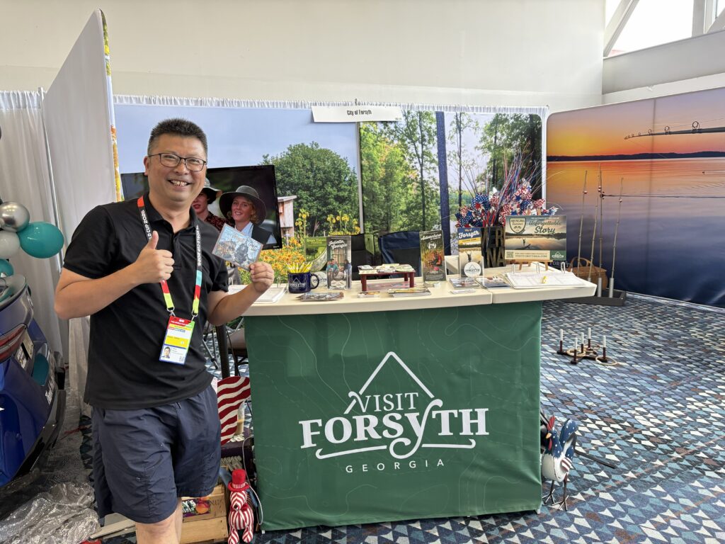 Reporter poses in front of Visit Forsyth GA booth