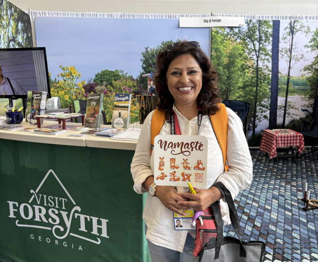 Journalist from India poses with Namaste Forsyth fan in front of Visit Forsyth GA booth