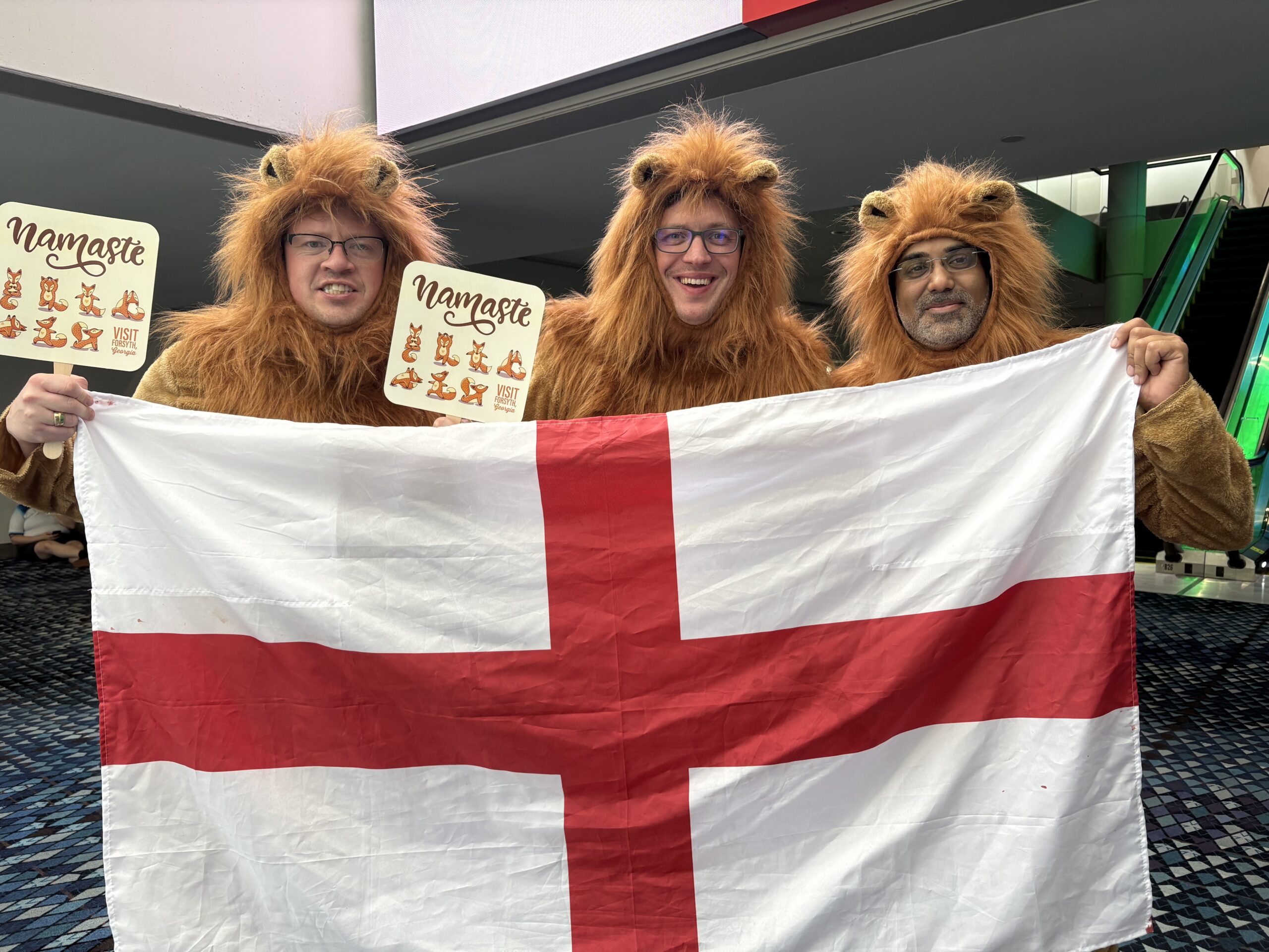three guys in lions costumes hold up English flag and Namaste fan