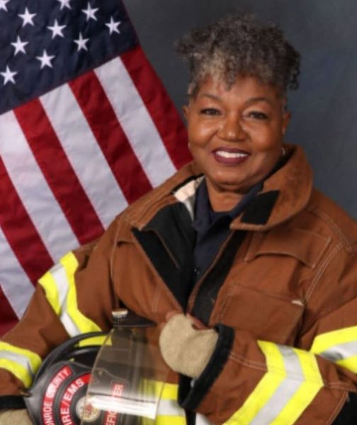 african american woman with short curly gray hair poses in firefighter uniform in front of american flag